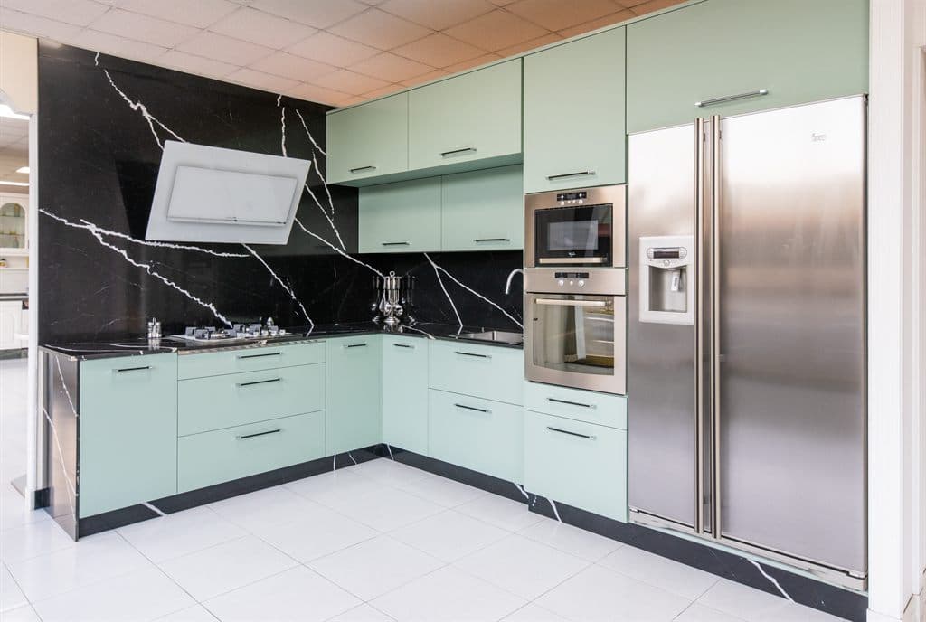 Cocina a medida en L con frentes verde agua y encimera de mármol negro en Noia